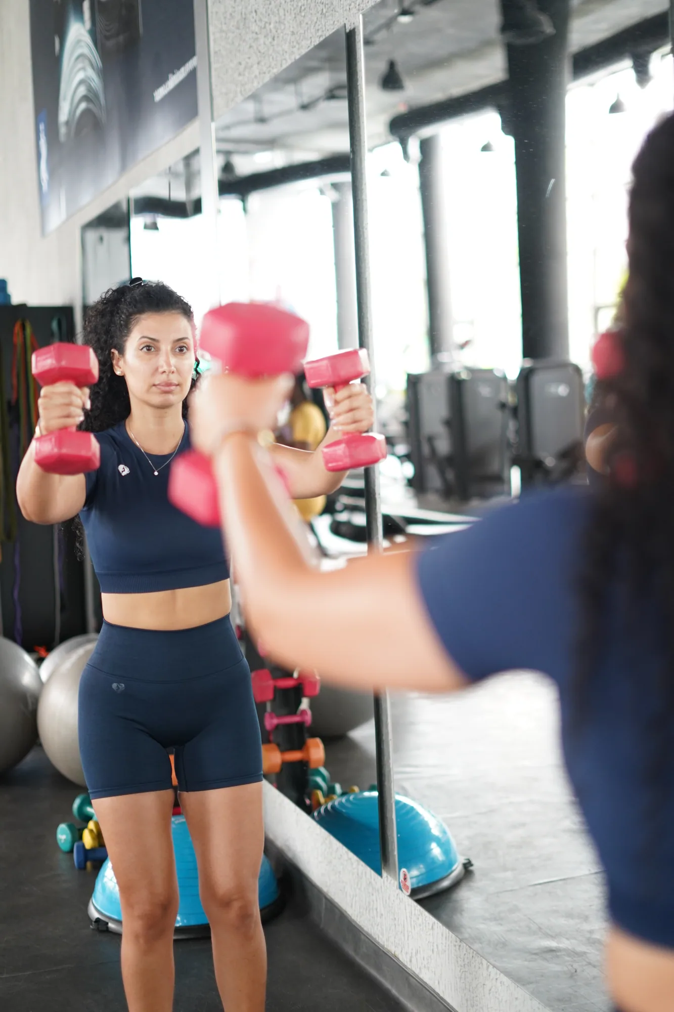 Ceece raising dumbbells in front of a gym mirror