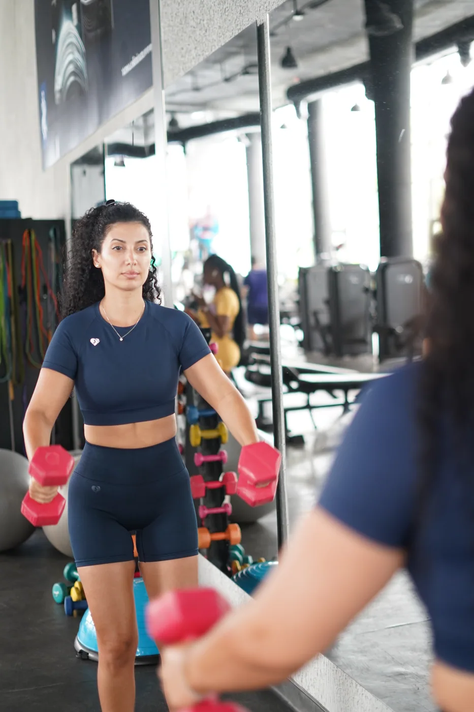 Ceece holding dumbbells in front of a gym mirror